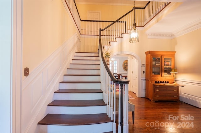 staircase featuring a high ceiling, ornamental molding, and hardwood / wood-style floors