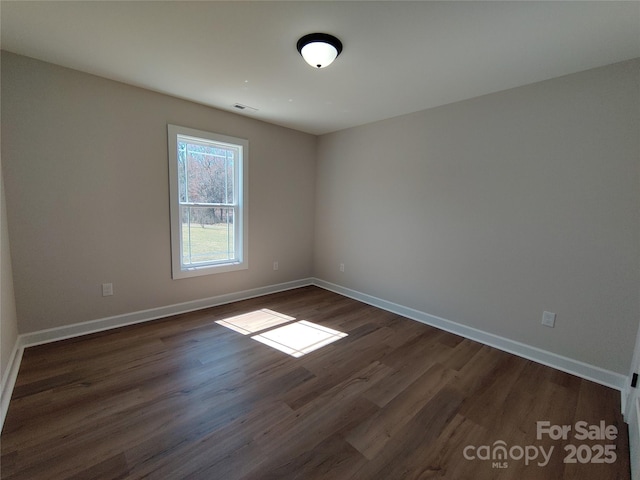 unfurnished room with dark wood-style floors, visible vents, and baseboards