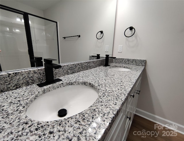 full bath with double vanity, baseboards, a sink, and wood finished floors