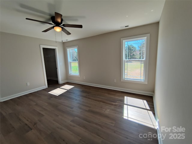 unfurnished room with dark wood finished floors, baseboards, visible vents, and ceiling fan