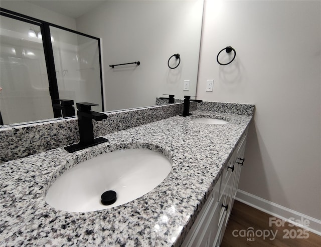 full bath with double vanity, wood finished floors, baseboards, and a sink