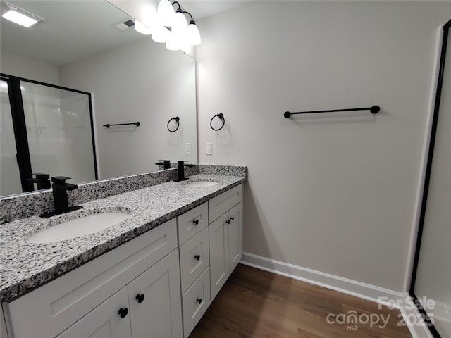 full bath with double vanity, a sink, a stall shower, and wood finished floors