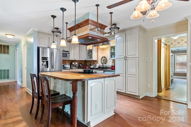 kitchen with pendant lighting, appliances with stainless steel finishes, ornamental molding, a kitchen island, and wood counters