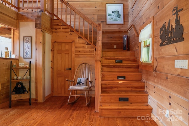 stairs featuring wood walls, a healthy amount of sunlight, a towering ceiling, and wood-type flooring