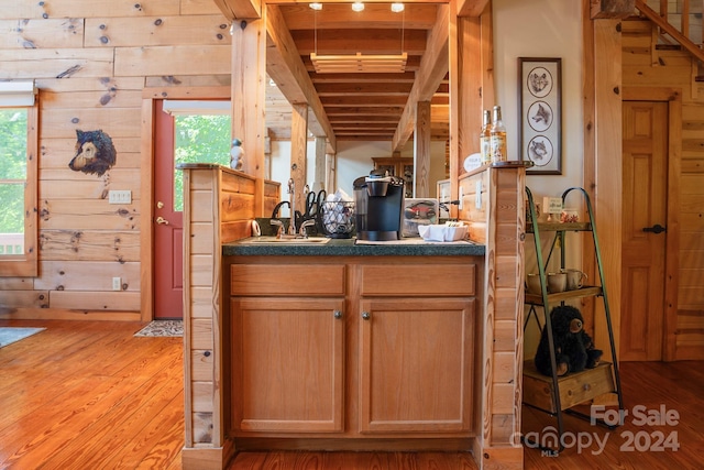 kitchen with light hardwood / wood-style floors, sink, beamed ceiling, and wooden walls