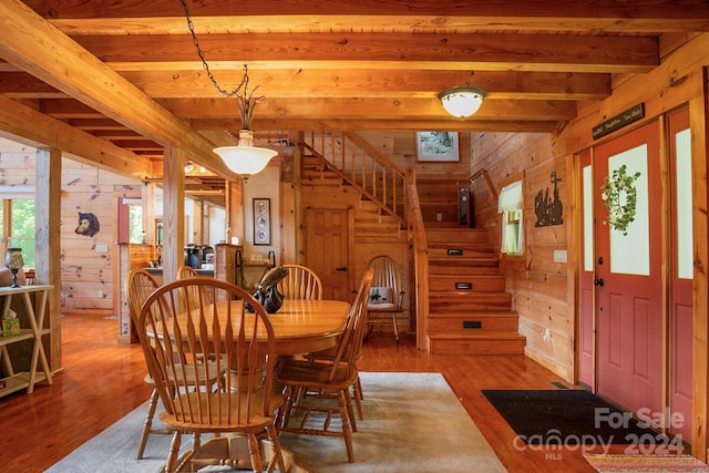 dining area with light hardwood / wood-style floors, beamed ceiling, and wooden walls