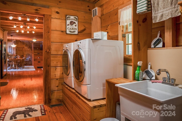 laundry area with washing machine and dryer, sink, wooden walls, and hardwood / wood-style floors