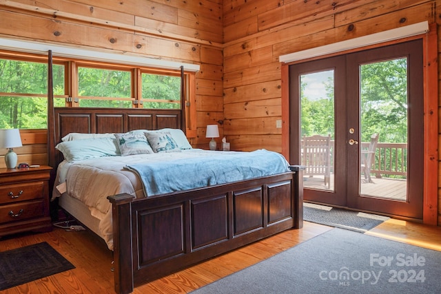 bedroom with access to exterior, french doors, wood walls, and light hardwood / wood-style flooring