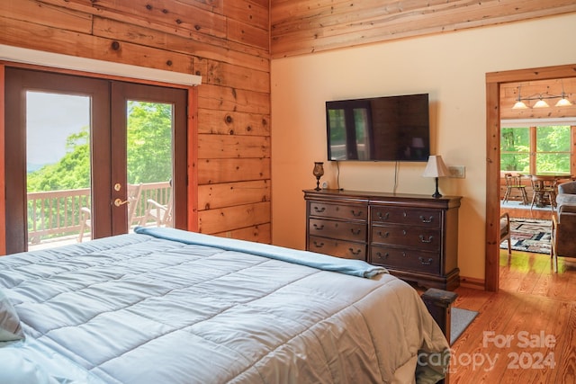 bedroom featuring french doors, access to exterior, light hardwood / wood-style floors, and wood walls