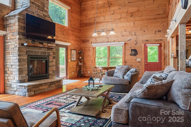 living room with wooden walls, a high ceiling, a stone fireplace, and wood finished floors