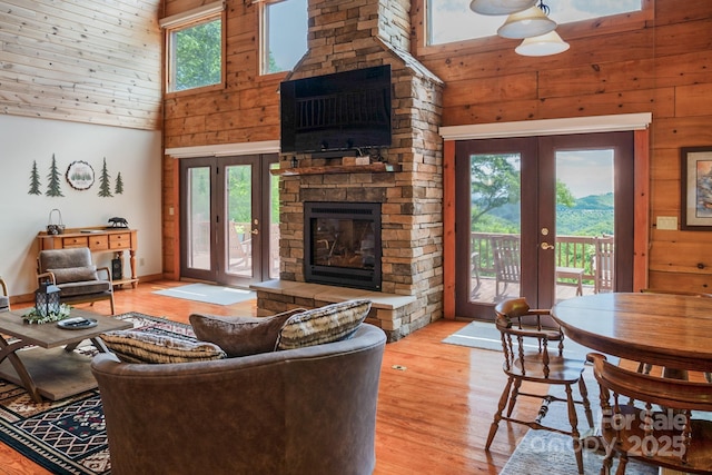 living room featuring french doors, a towering ceiling, wooden walls, and a fireplace