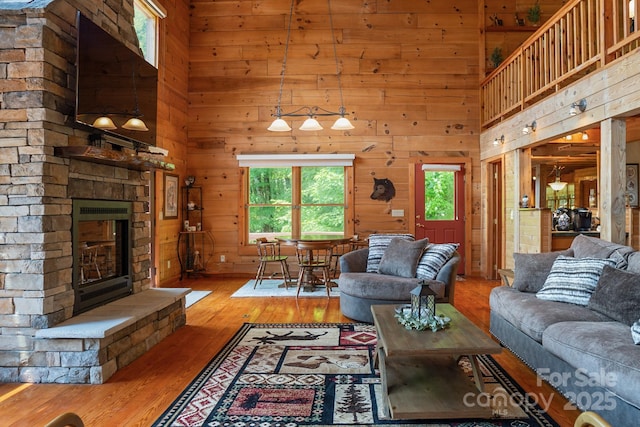 living area with a stone fireplace, wood walls, a high ceiling, and hardwood / wood-style floors