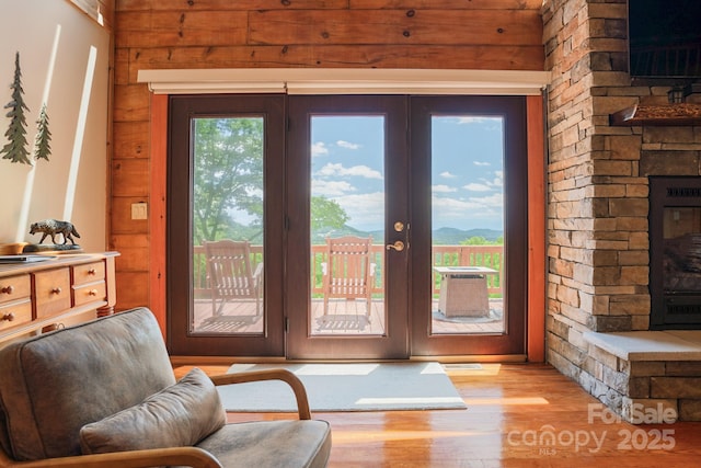 doorway to outside featuring a stone fireplace, french doors, wood walls, and wood finished floors