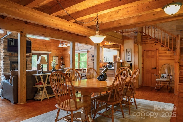 dining area with a fireplace, wood walls, beam ceiling, and wood finished floors