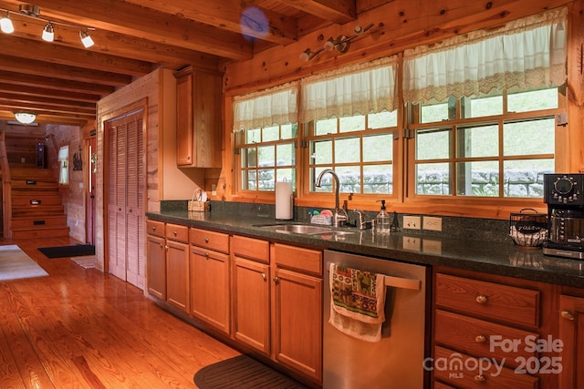 kitchen featuring a sink, light wood finished floors, dishwasher, dark stone countertops, and beamed ceiling