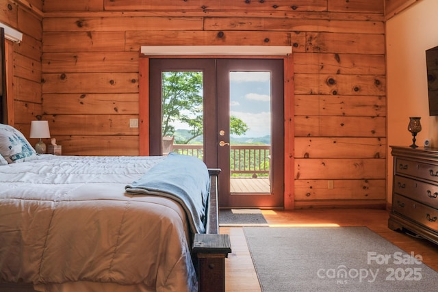 bedroom with access to outside, wood walls, wood finished floors, and french doors