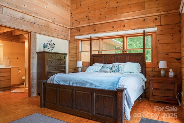 bedroom with wood walls, light wood-style flooring, and ensuite bath