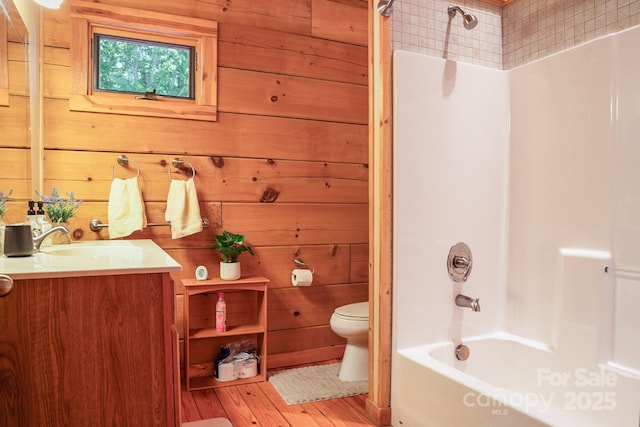 full bath featuring vanity, wood finished floors, toilet, wooden walls, and shower / washtub combination