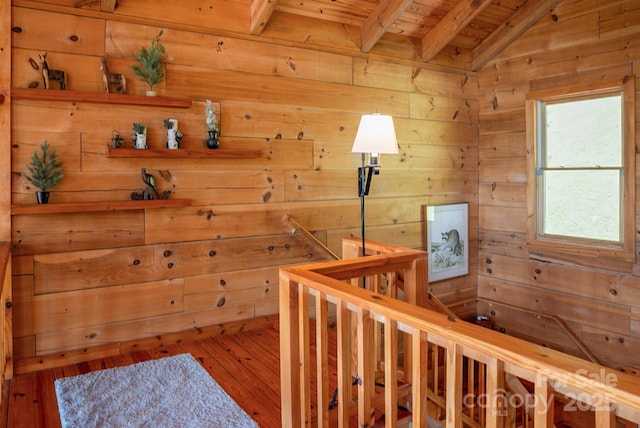 hallway with wood walls, lofted ceiling with beams, an upstairs landing, and wooden ceiling