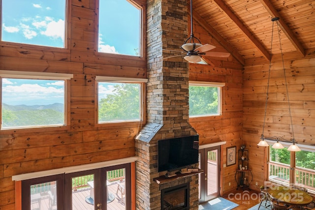 unfurnished living room featuring wood walls, beamed ceiling, high vaulted ceiling, wooden ceiling, and a ceiling fan