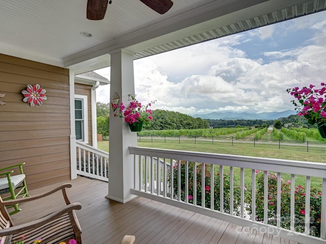 wooden terrace featuring ceiling fan, a mountain view, a rural view, and a porch