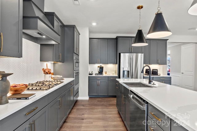 kitchen featuring custom exhaust hood, appliances with stainless steel finishes, dark hardwood / wood-style flooring, pendant lighting, and sink