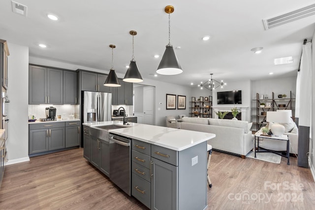 kitchen with appliances with stainless steel finishes, a kitchen island with sink, and gray cabinets