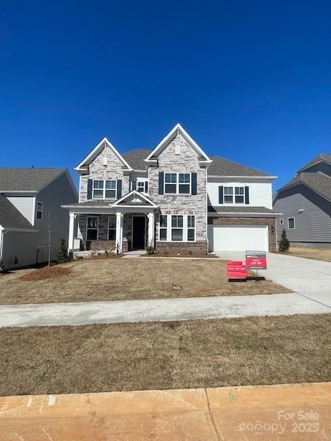 view of front of house featuring a porch, concrete driveway, a garage, stone siding, and a front lawn