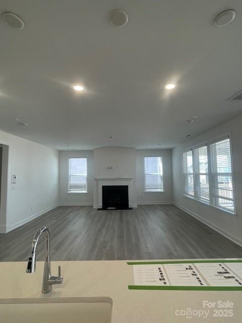 unfurnished living room featuring a healthy amount of sunlight, a fireplace with flush hearth, dark wood-style flooring, and a sink