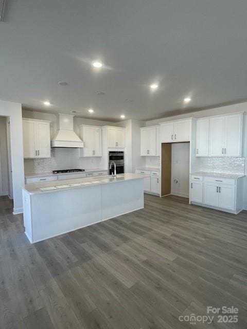 kitchen featuring white cabinets, premium range hood, and an island with sink