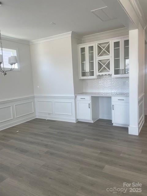 unfurnished dining area featuring dark wood-style floors, ornamental molding, a wainscoted wall, and a chandelier