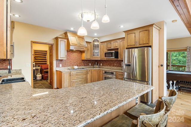 kitchen featuring light stone countertops, pendant lighting, appliances with stainless steel finishes, kitchen peninsula, and a breakfast bar area