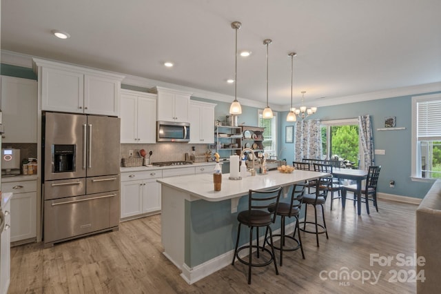 kitchen with white cabinetry, appliances with stainless steel finishes, an island with sink, and hanging light fixtures