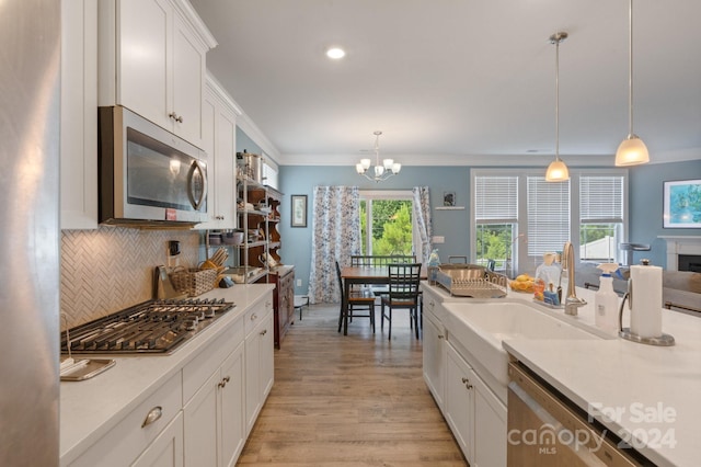 kitchen with appliances with stainless steel finishes, pendant lighting, sink, white cabinets, and light hardwood / wood-style floors