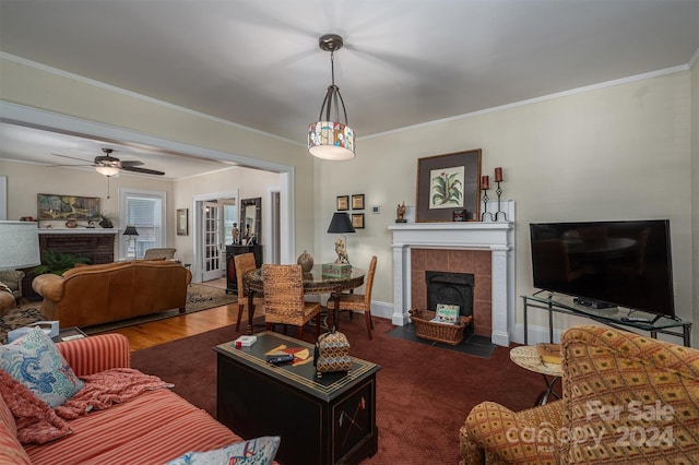 living room with ceiling fan, dark wood-type flooring, crown molding, and a fireplace