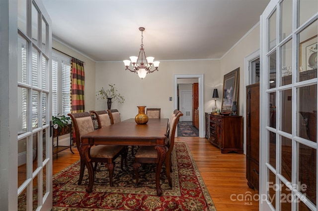 dining area with crown molding, light hardwood / wood-style flooring, french doors, and a notable chandelier