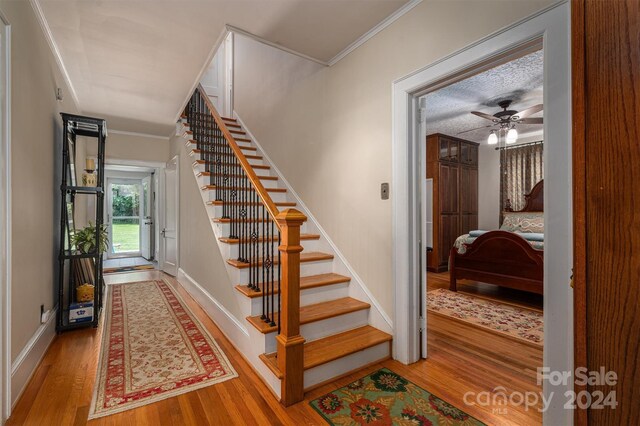 staircase with a textured ceiling, ceiling fan, crown molding, and hardwood / wood-style floors