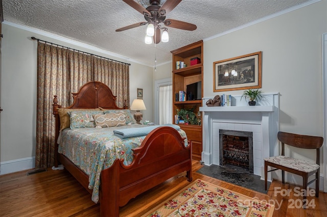 bedroom with a textured ceiling, hardwood / wood-style flooring, ornamental molding, ceiling fan, and a tiled fireplace