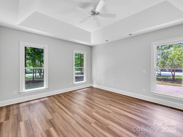 unfurnished room featuring ceiling fan, light hardwood / wood-style floors, and a tray ceiling