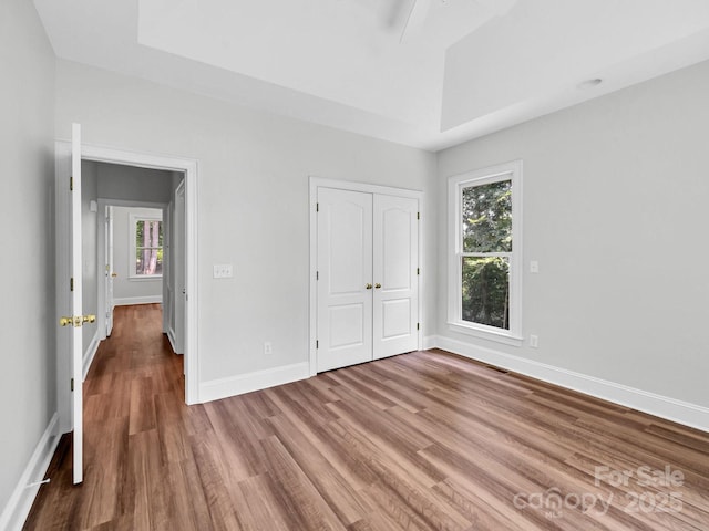 unfurnished bedroom featuring hardwood / wood-style flooring, a tray ceiling, and a closet