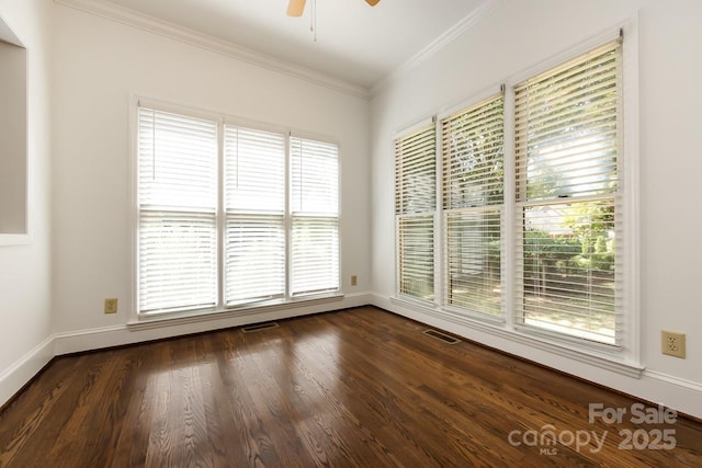 empty room featuring ceiling fan, a healthy amount of sunlight, dark wood-type flooring, and crown molding