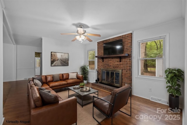 living room featuring ceiling fan, ornamental molding, wood-type flooring, and a brick fireplace