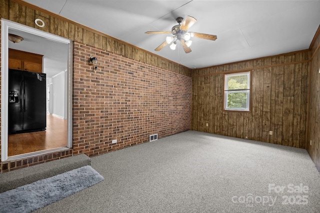 spare room featuring brick wall, carpet flooring, ceiling fan, and wood walls