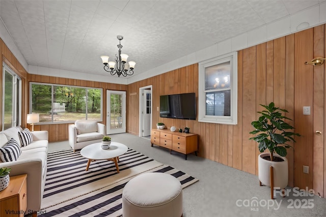 living room featuring carpet floors, a notable chandelier, and wood walls