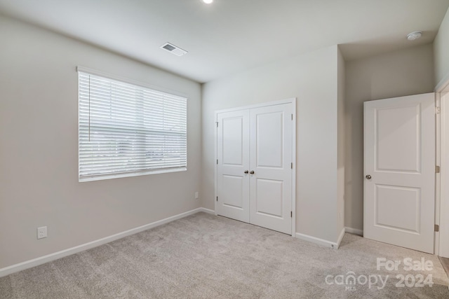 unfurnished bedroom with light colored carpet and a closet