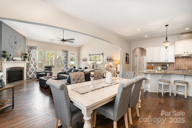 dining room featuring ceiling fan, dark hardwood / wood-style floors, a fireplace, and vaulted ceiling