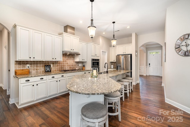 kitchen featuring white cabinetry, hanging light fixtures, a breakfast bar area, a center island with sink, and appliances with stainless steel finishes