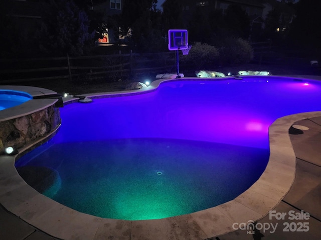 pool at night featuring an in ground hot tub