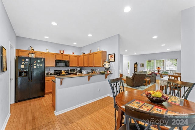 kitchen with a kitchen breakfast bar, kitchen peninsula, light wood-type flooring, and black appliances