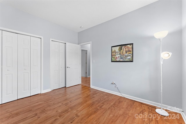 unfurnished bedroom featuring wood-type flooring and multiple closets